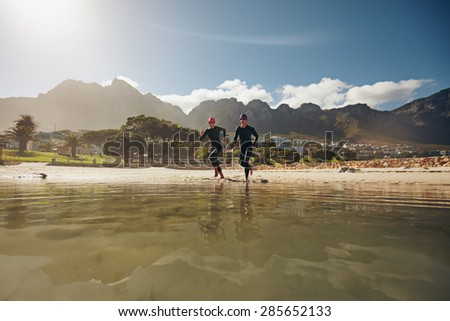 Shot of two athletes running into the water, practicing for triathlon competition. Young man and woman in wet suits preparing for the race at the lake.
