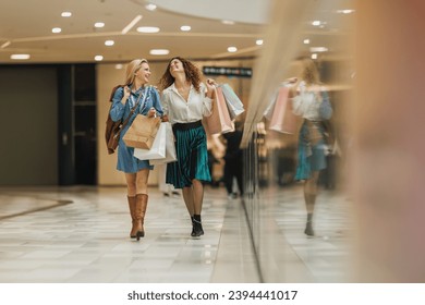 Shot of two attractive girlfriends smiling while walking with shopping bags in the city mall during the day. - Powered by Shutterstock