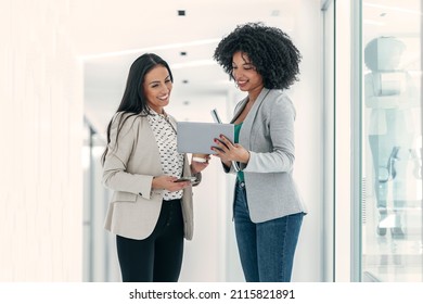 Shot Of Two Attractive Young Business Women Working With Digital Tablet While Talking And Walking In A Modern Startup. 