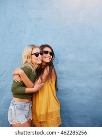 Shot Of Two Best Friends Embracing Over Blue Wall. Young Women Having Great Time Together.