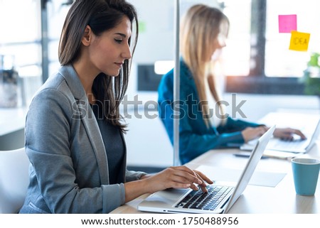 Shot of two business women work with laptops on the partitioned desk in the coworking space. Concept of social distancing.
