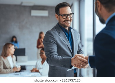 Shot of two businessmen shaking hands in an office. Two smiling businessmen shaking hands while standing in an office. Business people shaking hands, finishing up a meeting - Shutterstock ID 2265937125