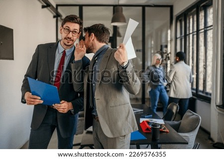 Shot of two coworkers gossiping and having a discussion in a modern office. Businessmen in meeting check the paperwork and discuss business strategy. Confident business people working together