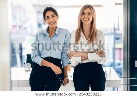Shot of two elegant attractive businesswomen working while looking at camera in a modern startup