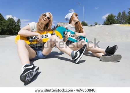 Shot of two girls sitting on a ground and holding their skateboards like the guitar