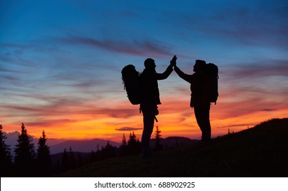 Shot Of Two Hikers High Fiving Standing On Top Of A Mountain With Their Backpacks Copyspace Beautiful Sunset On The Background Anonymous Achievement Gesture Celebrating Hiking Silhouette.