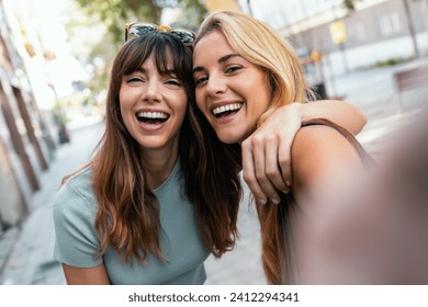 Shot of two joyful woman taking a selfie with smartphone while showing peace gesture in the city at night - Powered by Shutterstock