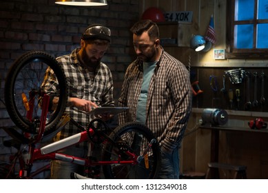 Shot of two mechanic discussing a problem behind a bicycle in a workshop using digital pad