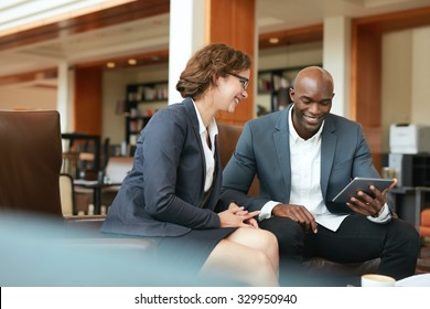 Shot Of Two People Looking At Something On A Touchscreen Computer. Smiling Business People Using Digital Tablet While Sitting At Coffee Shop.
