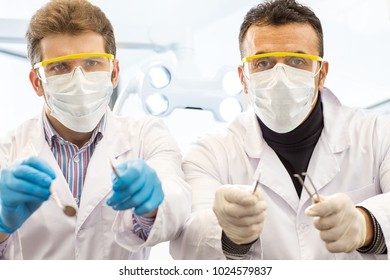 Shot Of Two Professional Dentists Wearing Medical Masks And Glasses Holding Out Dental Tools To The Camera Medicine Examination Checkup Dentistry POV Point Of View Service Stomatology.