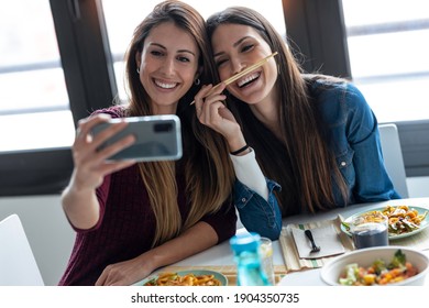 Shot of two smiling beautiful women friends eating japan food whiletaking a selfie with smart phone in the kitchen at home. - Powered by Shutterstock