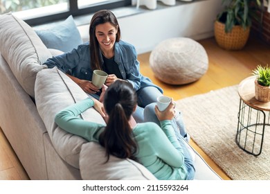 Shot of two smiling young women talking while drinking coffee sitting on couch in the living room at home. - Powered by Shutterstock