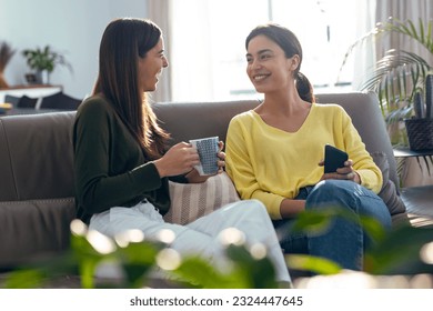 Shot of two smiling young women talking while drinking coffee sitting on couch in the living room at home. - Powered by Shutterstock