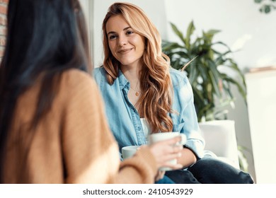 Shot of two smiling young women talking while drinking coffee sitting on couch in the living room at home. - Powered by Shutterstock