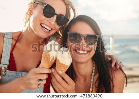 Shot of two young friends enjoying ice cream together on a summer day outdoors. Close up of cheerful female buddies eating icecream.