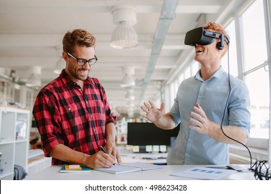 Shot of two young man standing at a table with VR goggles and writing on notepad. Developers testing virtual reality glasses in office. - Powered by Shutterstock