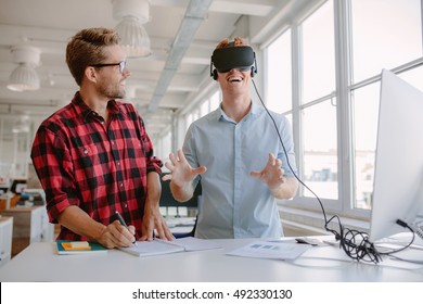 Shot of two young men testing virtual reality glasses in office. Businessman wearing VR goggles and colleague writing notes. - Powered by Shutterstock