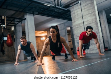 Shot of two young men and a woman standing in plank position at the gym - Shutterstock ID 1127058125
