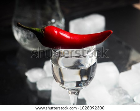 a shot of vodka, an alcoholic beverage, next to ice, fire, ice, red chili pepper. The concept of alcohol, spirits