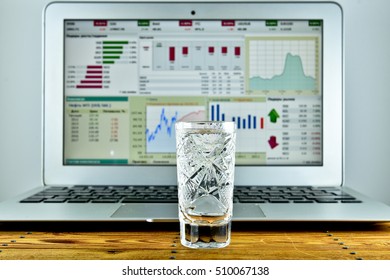 A Shot Of Vodka In Front Of A Laptop With A Stock Ticker On The Screen On Wood Table