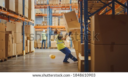Shot of a Warehouse Worker Has Work Related Accident. He is Falling Down BeforeTrying to Pick Up Heavy Cardboard Box from the Shelf. Hard Injury at Work.