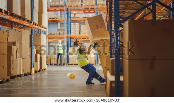 Shot of a Warehouse Worker Has Work\
Related Accident. He is Falling Down BeforeTrying to Pick Up Heavy\
Cardboard Box from the Shelf. Hard Injury at\
Work.