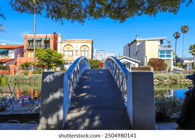 a shot of a white wooden bridge over the canal water with lush green trees and plants reflecting off the water with blue sky at the Venice Canals in Venice, Los Angeles California USA	 - Powered by Shutterstock