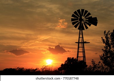 A shot of a Windmill Silhouette with a bright orange Sunset in the back ground  with tree silhouettes north of Hutchinson Kansas.