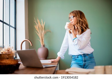 Shot of woman drinking her coffee while standing in the kitchen at home before starting working from home. Home office.  - Powered by Shutterstock