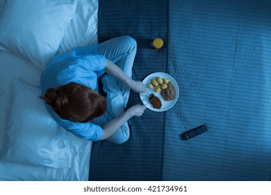 Shot Of A Woman Sitting On A Bed And Eating Dinner