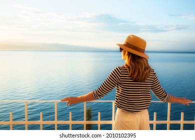 Shot of woman wearing straw hat and sunglasses while standing on balcony and looking at sea view. Daydreaming. - Shutterstock ID 2010102395