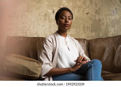 A shot of a young African American woman sitting confidently on the leather sofa. - Powered by Shutterstock