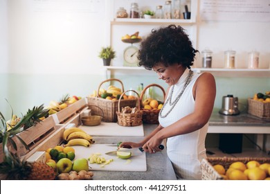 Shot of young african woman working at juice bar and cutting fruits. Female bartender making fresh juice. - Powered by Shutterstock