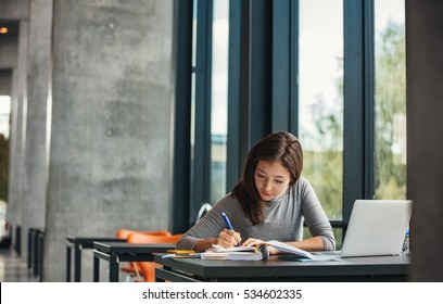 Shot of young asian female student sitting at table and writing on notebook. Young female student studying in library. - Powered by Shutterstock