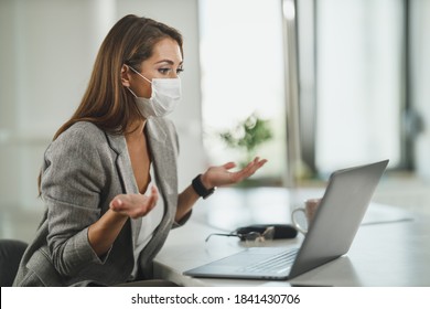 Shot of a young business woman with protective mask sitting alone in her office and working on laptop during corona virus pandemic. - Shutterstock ID 1841430706