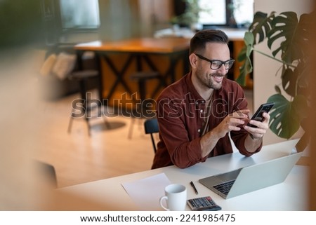 Shot of a young businessman using a smart phone in a home office. Smiling, touching the screen, browsing the internet.