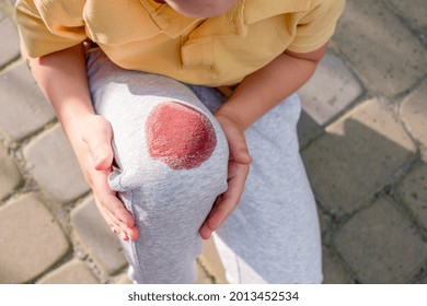 Shot Of A Young Child With A Knee Injury On The Street During The Day. Photo Of Boy Holding His Knee While Falling In Sidewalks. High Quality Photo