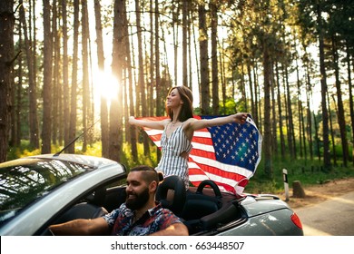 Shot of a young couple enjoying riding in a car. Focus on the woman who is holding an american flag. - Powered by Shutterstock