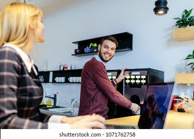 Shot of a young couple talking in an office cafeteria. Man making a coffee. - Powered by Shutterstock