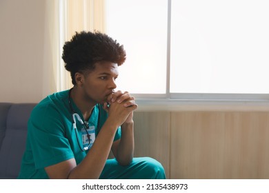 Shot Of A Young Doctor Looking Distressed. Tired Exhausted Male African Scrub Nurse Wears Green Uniform Gloves Sits On Hospital. Depressed Sad Black Ethic Doctor Feels Burnout Stress