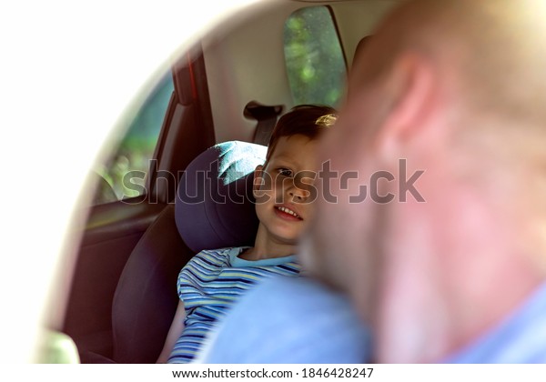 Shot of a young father is turning around from the\
driving seat of his car to check on cute little son who is in a\
safety seat in the back. Dad and son smiling to each other and\
having fun in the car.