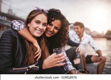 Shot Of Young Female Friends Having Fun With Drinks On The Lake. Group Of People Enjoying A Day By The Lake.