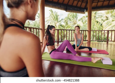 Shot of young female relaxing on yoga mat and talking after workout session. Female friends during yoga class break at fitness center. - Powered by Shutterstock