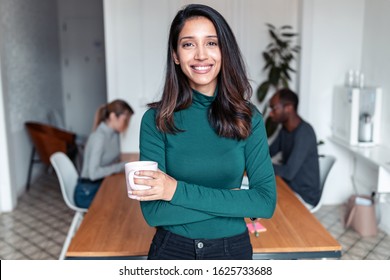 Shot of young indian business woman entrepreneur looking at camera in the office. In the background, her colleagues working.