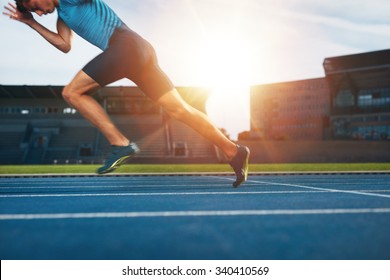 Shot Of Young Male Athlete Launching Off The Start Line In A Race. Runner Running On Racetrack In Athletics Stadium.