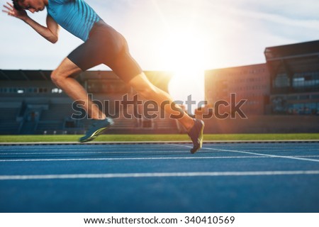 Shot of young male athlete launching off the start line in a race. Runner running on racetrack in athletics stadium.