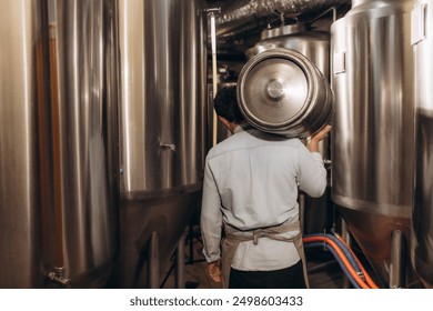 Shot of young man with metal beer barrels at brewery. Brewer carrying keg at brewery plant. - Powered by Shutterstock