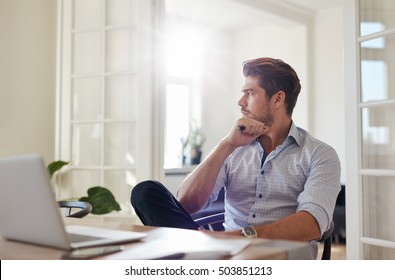 Shot of young man sitting at table looking away and thinking. Thoughtful businessman sitting home office. - Powered by Shutterstock