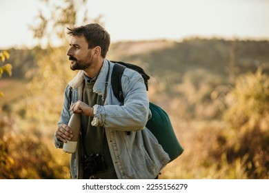 Shot of a young man taking a break while out on a hike. Man about to open a water bottle and looking at the landscape  - Powered by Shutterstock