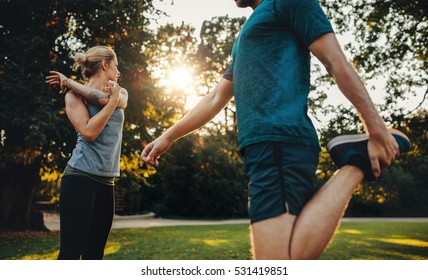 Shot Of Young Man And Woman Doing Stretching Exercise In The Park. Young Couple Warming Up For Morning Workout.